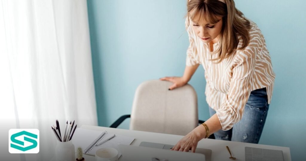 Choosing the Best UAE Free Zone for an AI Startup in 2026 - woman standing at a desk using a laptop with notepad and coffee